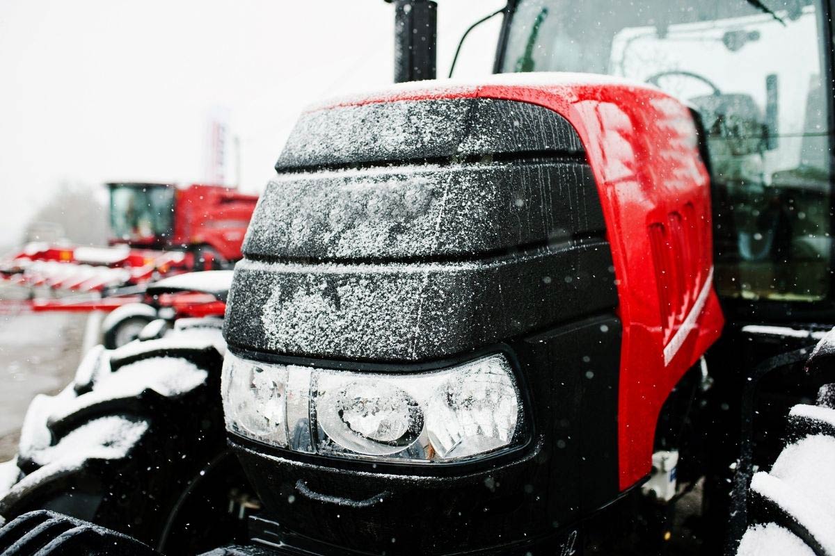 Up close picture taken of a red tractor that is dusted in snow