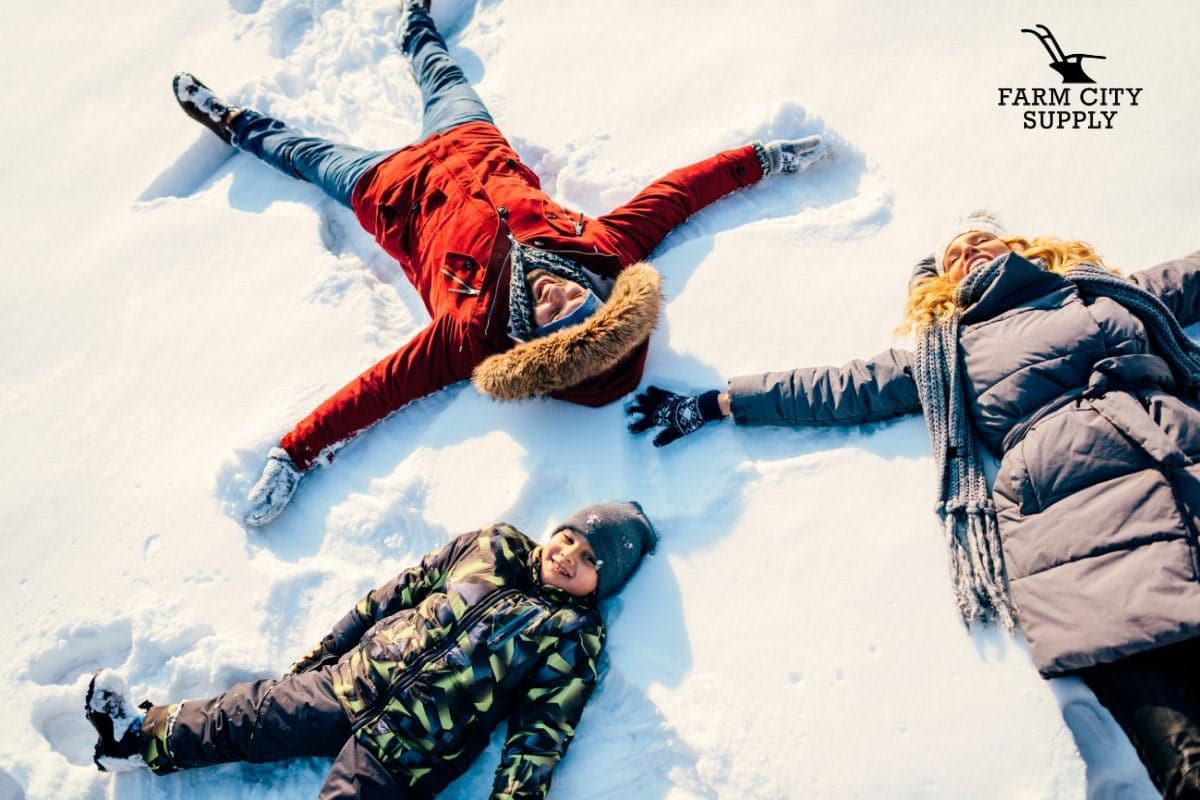 Kids laying on fresh snow wearing winter gear making snow angels