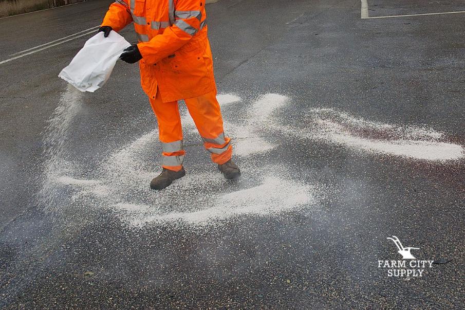 Worker in safety gear spreading salt across a parking lot for winter ice control.