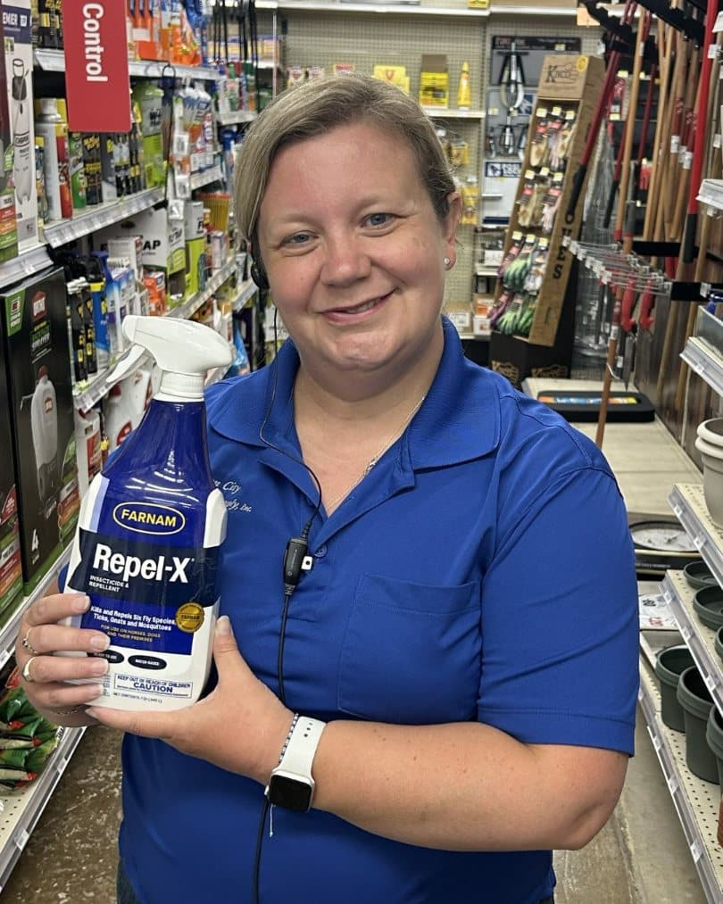Farm City Supply employee holding a bottle of Farnam Repel-X insecticide and repellent in a store aisle.