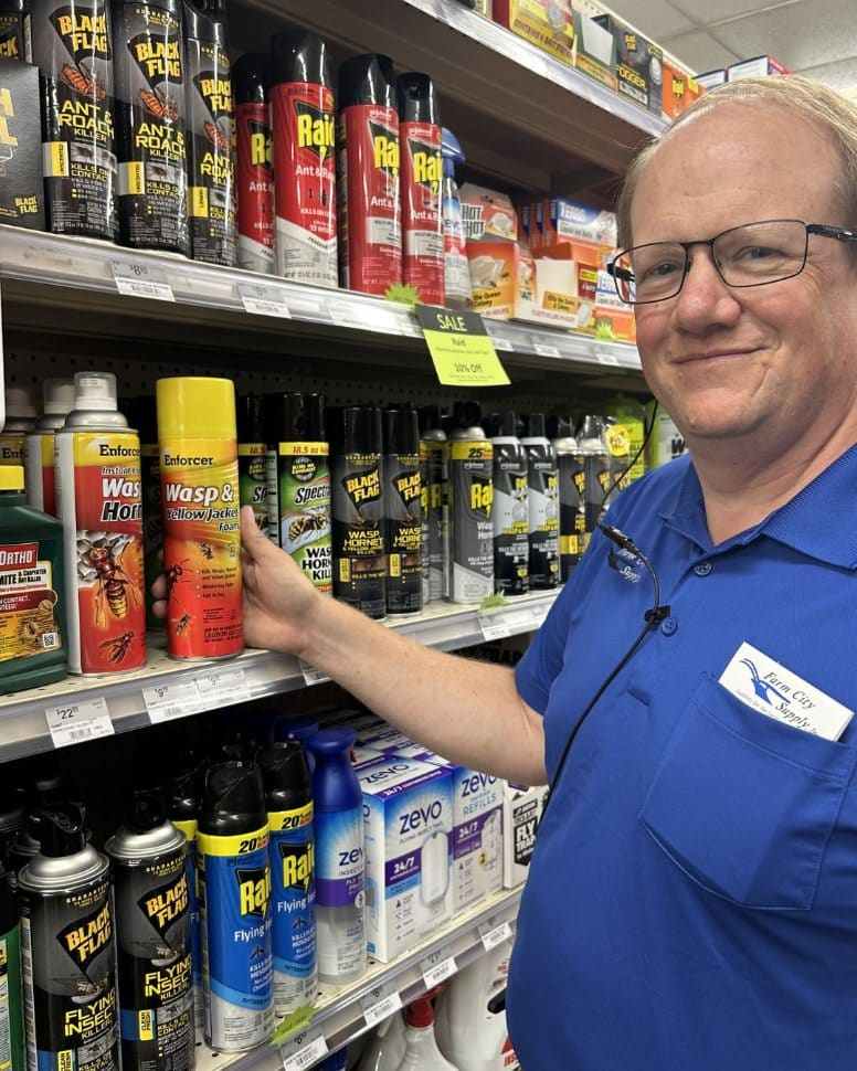 Farm City Supply employee pointing to Enforcer Wasp and Yellow Jacket Killer on a stocked pest-control shelf.