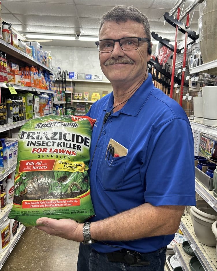 Farm City Supply employee holding a bag of Spectracide Triazicide Insect Killer for Lawns in the pest-control aisle.