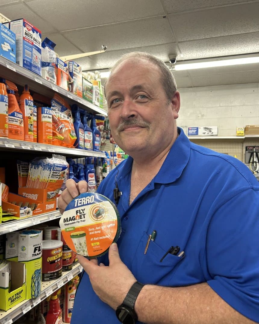 Farm City Supply employee displaying a TERRO Fly Magnet disposable fly trap beside a shelf of pest-control products.